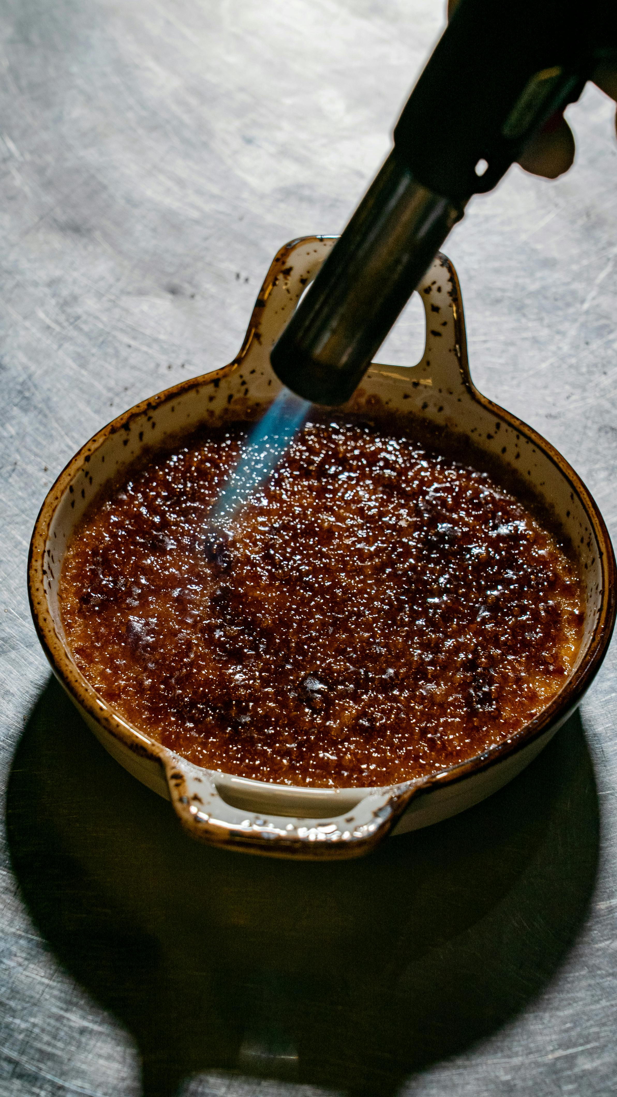 Crème brûlée being torched in a speckled ceramic ramekin