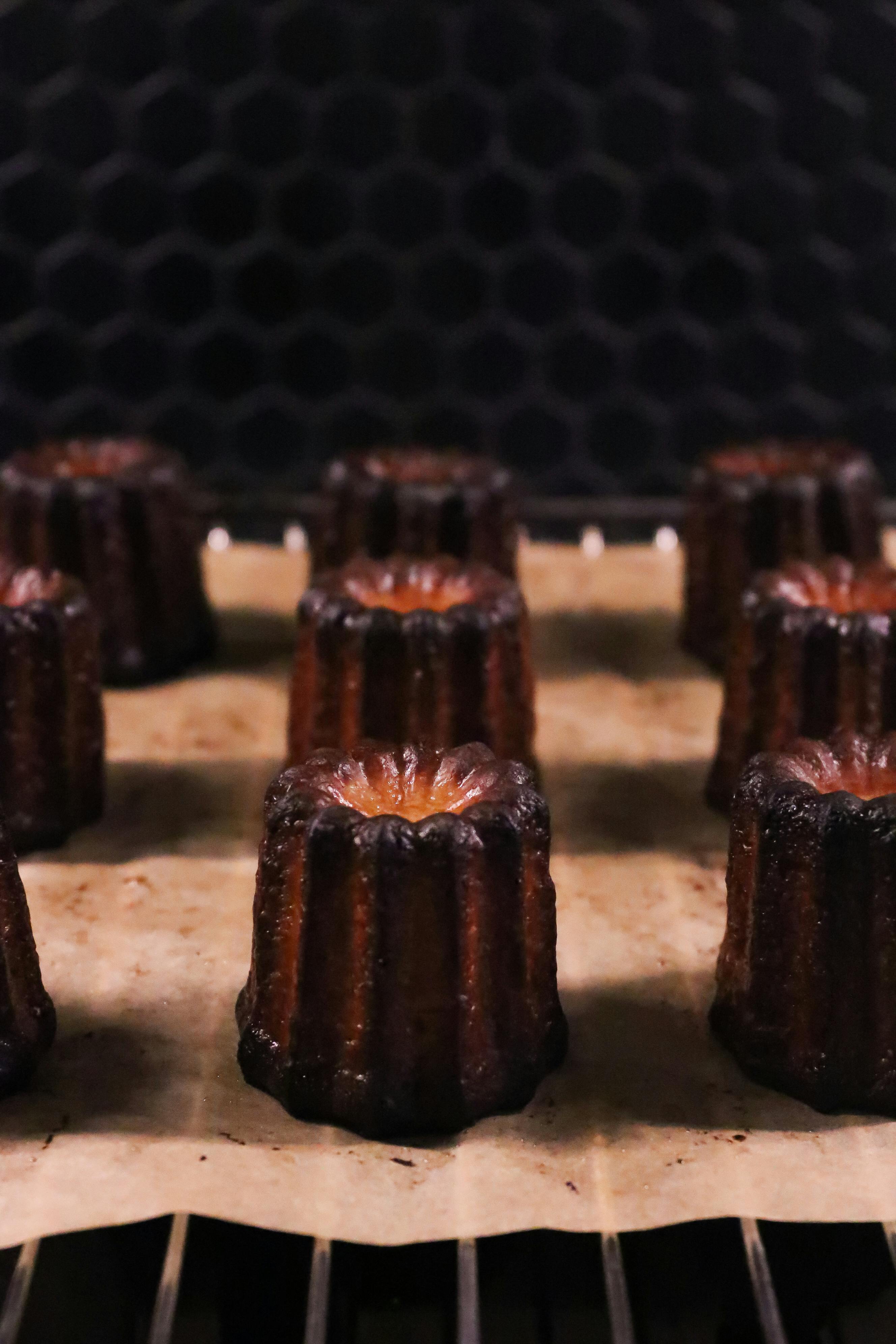 Dark caramelised canelés on parchment, side-lit