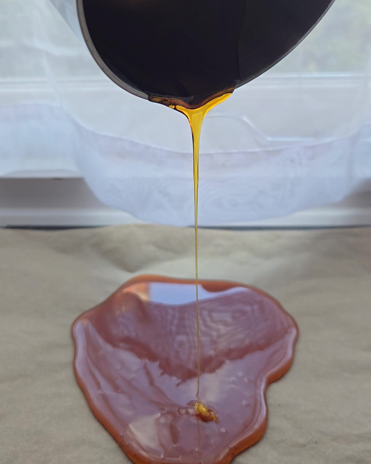 Molten caramel made with hush pouring from a pan in a thin amber thread into a glassy pool on baking parchment.