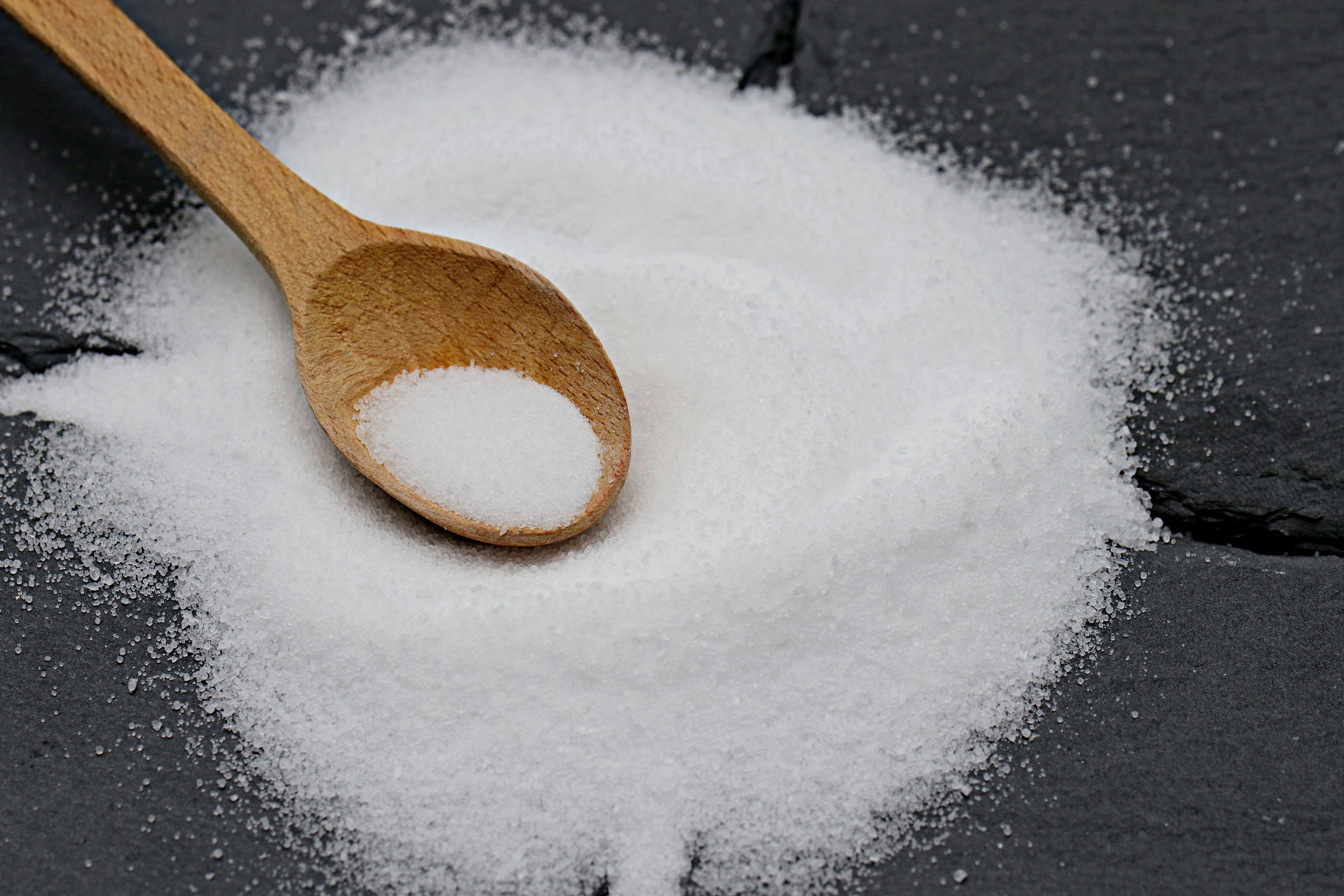 Side angle of white sugar with a wooden spoon on dark slate